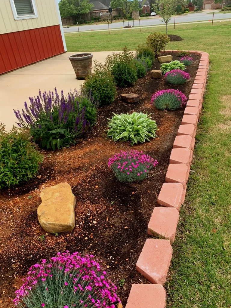 Backyard patio with landscaped hydrangeas, native flowers, mulched beds, and stone wall edging in Northwest Arkansas